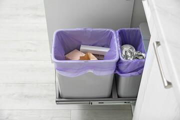 Fototapeta na wymiar Open cabinet with full trash bins for separate waste collection in kitchen