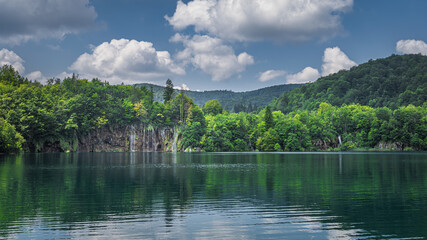 Fototapeta na wymiar Panoramic view on beautiful waterfalls with reflections in lake. Green lush forest, Plitvice Lakes National Park UNESCO World Heritage in Croatia