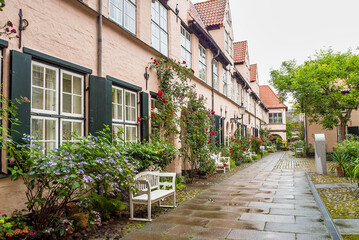 Fototapeta na wymiar Beautiful cozy courtyard with old houses and flowers in the street of old town Lubeck, Germany
