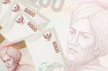 5000 Indonesian rupiah bills lies in stack on background of big semi-transparent banknote. Abstract...