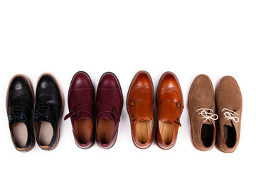 Bunch of different style men's shoes in a row. Close up shot chukka boots, single and double monk strap oxfords, brown, black and burgundy brogues. Top view, copy space, flat lay, white background
