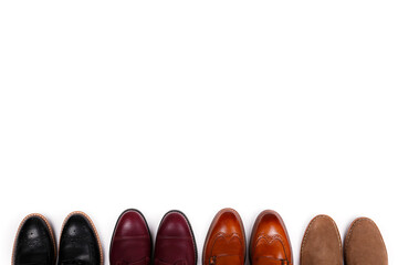 Bunch of different style men's shoes in a row. Close up shot chukka boots, single and double monk strap oxfords, brown, black and burgundy brogues. Top view, copy space, flat lay, white background