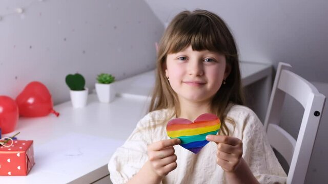 Valentine's Day. A cute Caucasian girl holding a rainbow-colored heart in front of her. Lgbt free love. Slow motions