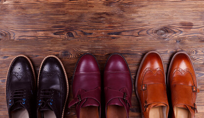 Bunch of different style men's shoes in a row. Close up shot chukka boots, single and double monk strap oxfords, brown, black and burgundy brogues. Top view, copy space, flat lay, wooden background