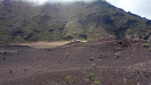 Drone flying fast over the volcanic land and crater landscape to rustic cabin in Haleakala National Park, Maui, Hawaii, USA. Outdoors adventure and nature travel. Old building in ancient volcanic peak