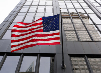 Large USA flag waving in front of a tall city building.