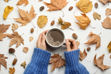 Woman with cup of hot drink at white wooden table, top view. Cozy autumn atmosphere