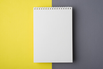 Above close up overhead view photo of clear notepad with spiral and copy space for design isolated half gray and bright trendy yellow desk