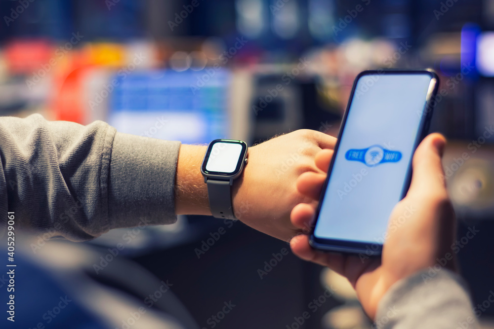Poster man holds a smartphone with a close-up wi-fi icon and a smart watch on his hand.