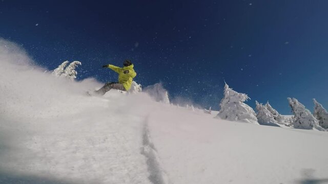 Snowboarder in a bright lime dressing riding backcountry in a front-facing tracking shot on a sunny winter day in the mountains