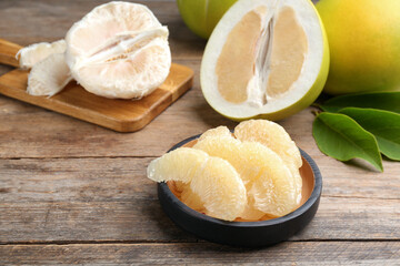 Bowl with peeled pomelo slices on wooden table, closeup