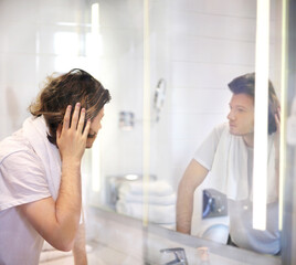 Fototapeta premium young man looking in the mirror,applying facial cream in bathroom while looking at mirror...