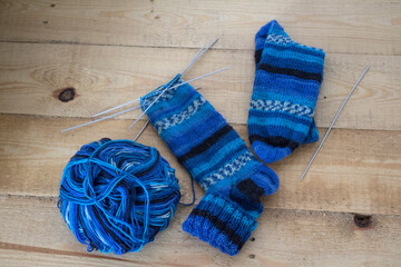 Knitting socks. Blue gradient yarn, knitting needles and two striped socks on wooden background. Hobbies and crafts concept. 
