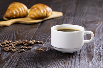 A cup of hot coffee and croissants on a wooden background. Breakfast with coffee and fresh pastry. Copy space. Fresh cake and pastry