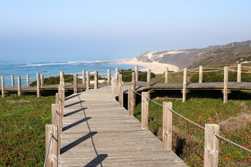 path made of wooden roasts, wooden bridge leading to the blue horizon over a sandy and overgrown cliff