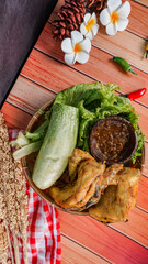 delicious fried chicken or ayam goreng, traditional fried chicken, chili sauce, and fresh vegetables, over wooden board, - selective focus