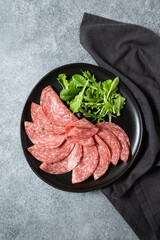 Traditional Italian salami on a black plate served with arugula and multi-grain baguette
