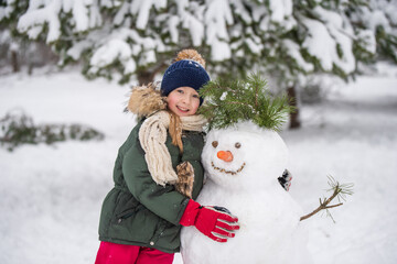 Happy child girl plaing with a snowman on a snowy winter walk