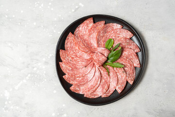 Traditional Italian salami on a black plate served with arugula and multi-grain baguette