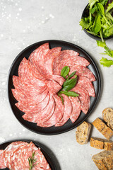 Traditional Italian salami on a black plate served with arugula and multi-grain baguette