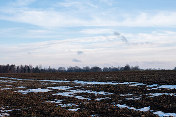 in early winter on a snowy white field there are many spots of brown earth