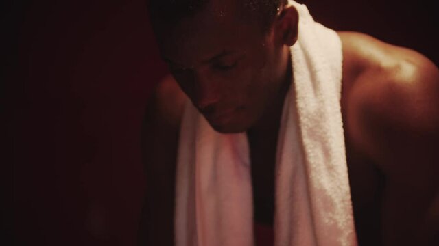 Black young man sits in a locker room with a towel around his neck - light reflecting differently
