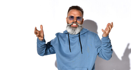 Naklejka premium Irritated emotional gray-haired bearded man in fashionable sunglasses, casual sweatshirt looks into the camera with irritation. People, negative emotions and feelings. Studio shot isolated on white