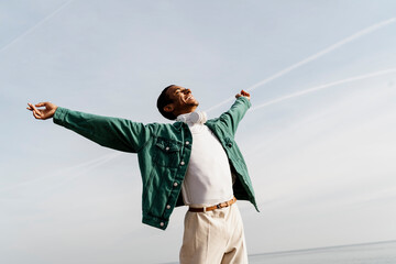 Happy carefree man with arms outstretched against sky