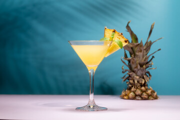 Refreshing pineapple cocktail with slice of pineapple and mint in front of shadow of palm leaves in a shining sun.