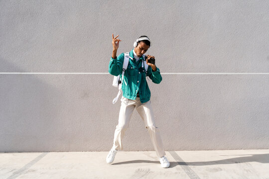 Carefree man with headphones and backpack singing while standing on footpath