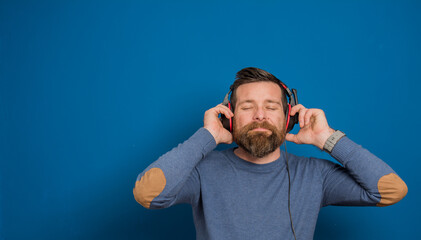 Naklejka premium Young man over isolated blue wall listening to music with headphones