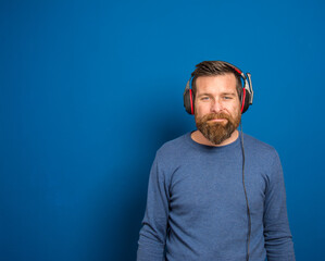 Fototapeta premium Young man over isolated blue wall listening to music with headphones