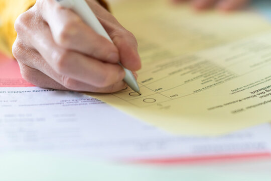 Close-up of woman with pen filling voting form at home