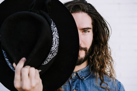 Handsome young man holding hat against white wall