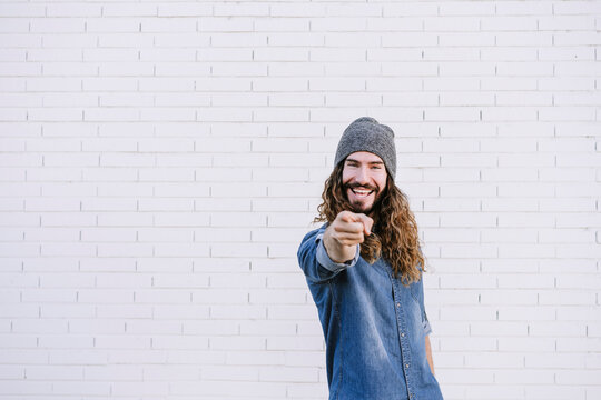 Handsome young man pointing while standing against brick wall