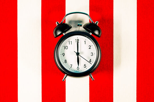 Alarm clock lying on white and red striped pattern