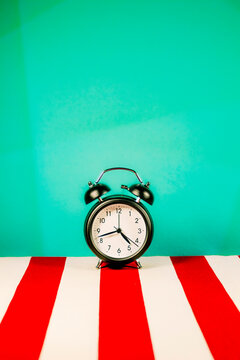 Studio shot of alarm clock standing on white and red striped pattern