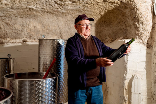 Senior male winemaker holding bottle of red wine at winery