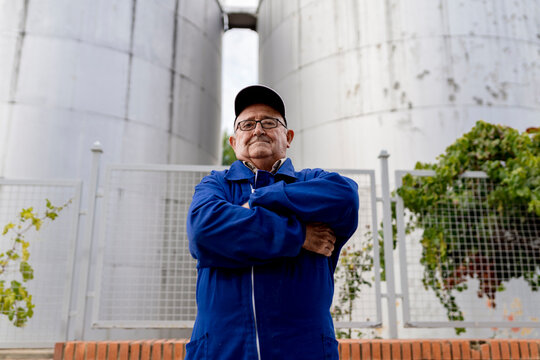 Elderly male winemaker with arms crossed against stainless steel vat at winery industry