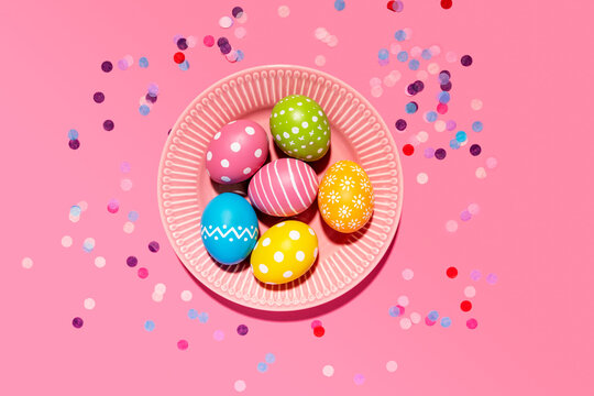 Colorful hand colored Easter eggs in tray with confetti on pink background