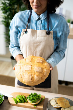 Mid section of young woman holding freshly baked loaf of bread