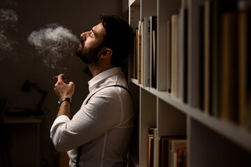 Portrait of bearded man smoking cigar in front of bookshelf