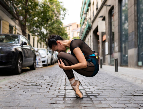 Ballet dancer wearing leotard crouching on footpath in city