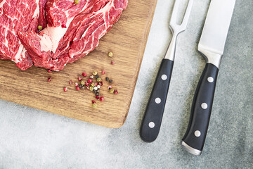 Fresh raw beef steaks with pepper on wooden cutting board board. Copy space, top view.
