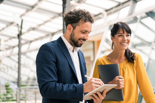 Smiling male colleague using digital tablet standing by female entrepreneur at office