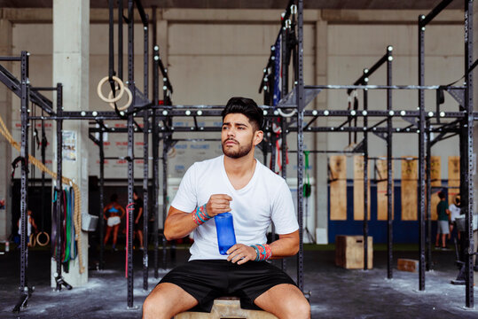 Young Man Holding Water Bottle While Sitting On Box At Gym