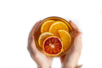 glass cup with tea from red and yellow oranges in female hands, top view, isolate on white