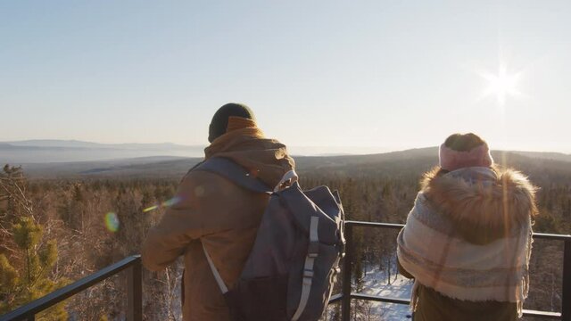 Medium back-view footage of couple standing at viewing point looking at beautiful wintery landscape and taking pictures on smartphones