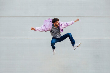 Young man jumping happily against wall