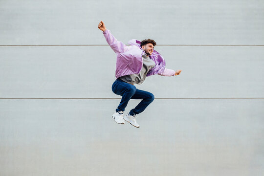 Carefree man with arms outstretched jumping against wall